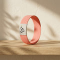 Coral-pink Daily Verse Bracelet standing on an oak shelf in warm morning light