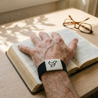 Black bracelet on a man's wrist resting on an open Bible